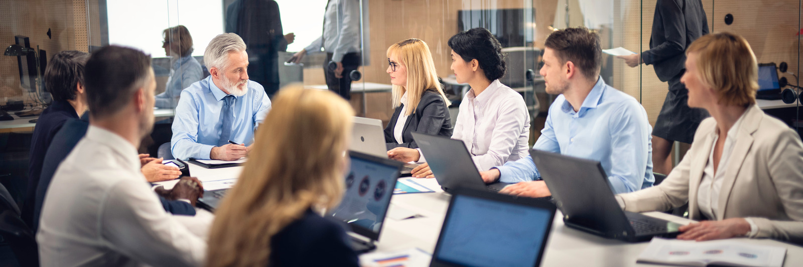 Group of businessmen and businesswomen sitting and talking at a table with laptops during a board meeting.